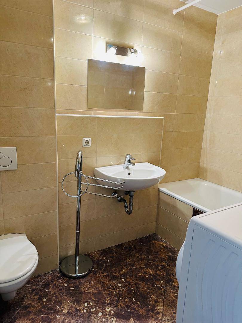 Badezimmer mit beigefarbenen Wandfliesen, dunklem Boden, Waschbecken, Toilette und Badewanne.