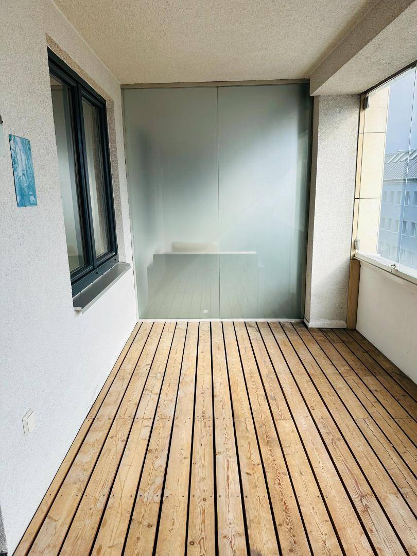 Heller Balkon mit Holzfußboden und Milchglas-Trennelement, das Privatsphäre und Sonnenschein bietet.