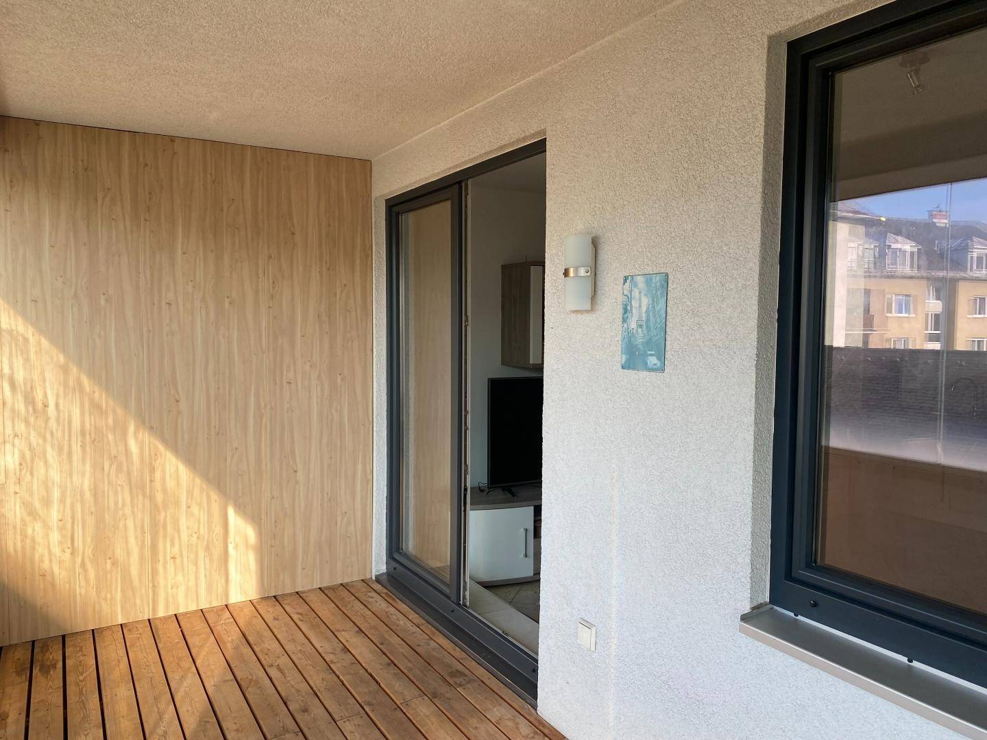 Sonniger Balkon mit Holzboden und Holzverkleidung, der Zugang zu den Innenräumen bietet.