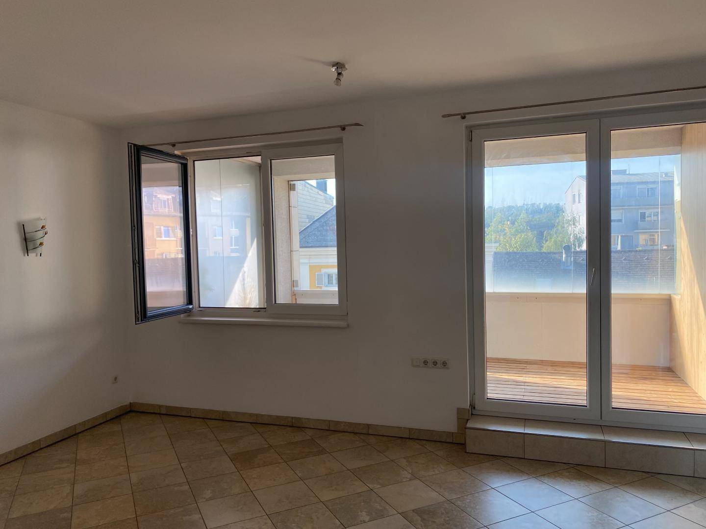 Helles Wohnzimmer mit Fliesenboden, großen Fenstern und direktem Zugang zu einem Balkon.