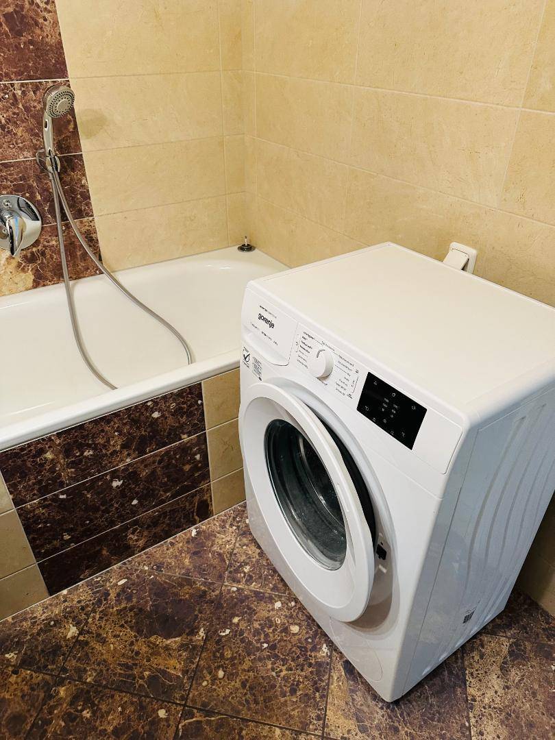 Badezimmer mit Badewanne inklusive Duschfunktion und einer praktischen Waschmaschine.