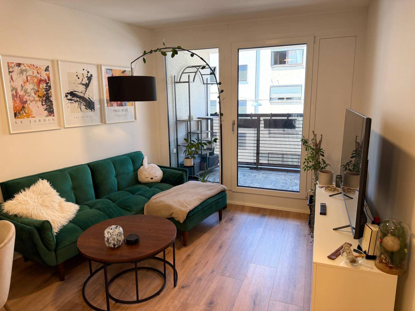 Helles Wohnzimmer mit grünem Sofa, Holzboden und Zugang zum Balkon.