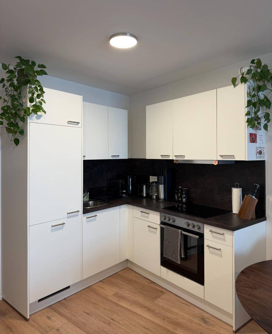 Moderne Einbauküche mit weißen Schränken, dunkler Arbeitsplatte und Laminatboden.