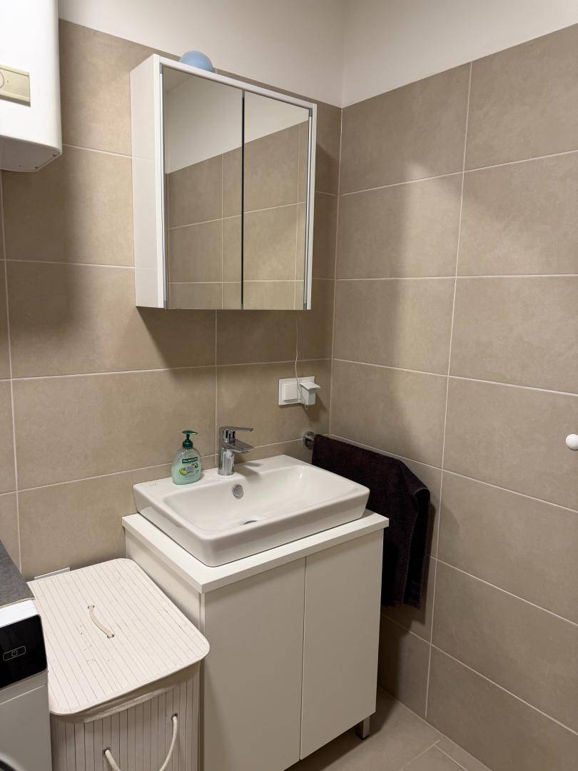 Badezimmer mit modernem Waschbecken, Spiegelschrank und beigefarbenen Fliesen.