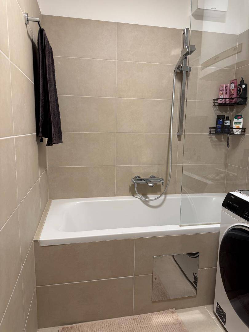 Badewanne mit Glasabtrennung und Duschfunktion in einem modern gefliesten Badezimmer.