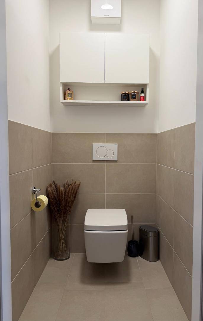 Separates WC mit wandhängender Toilette, Fliesen und praktischem Wandschrank.