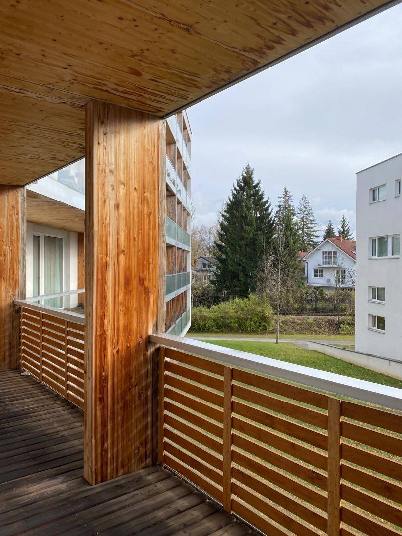 Geräumiger Holzbalkon mit Blick ins Grüne und auf die umliegenden Gebäude, sehr naturnah.