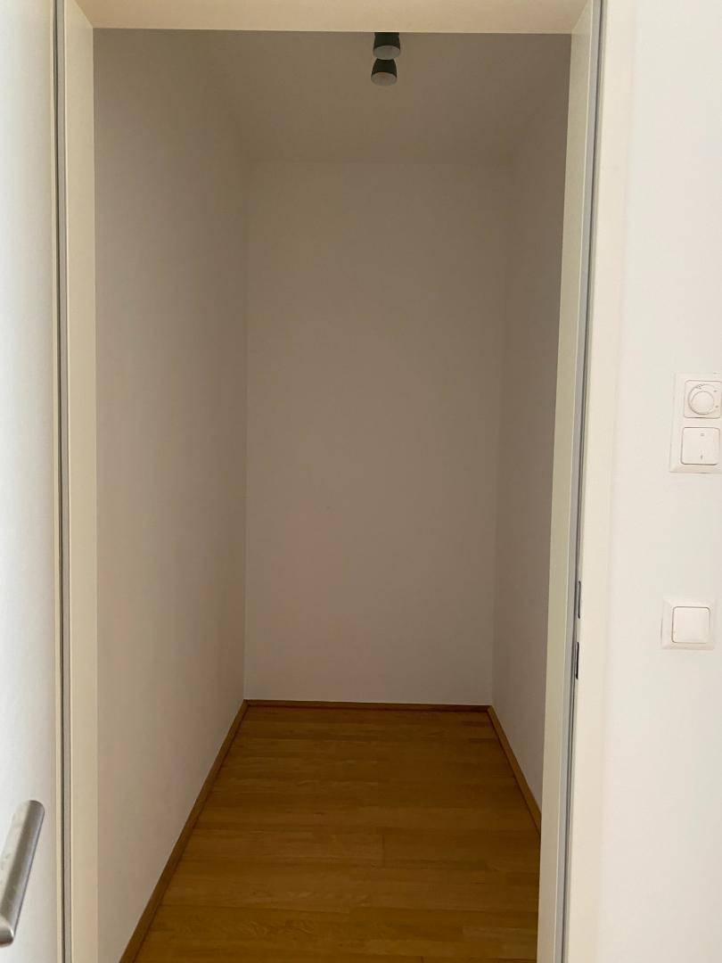 Leerer Abstellraum mit hellem Parkettboden und weißen Wänden, bietet viel Stauraum.