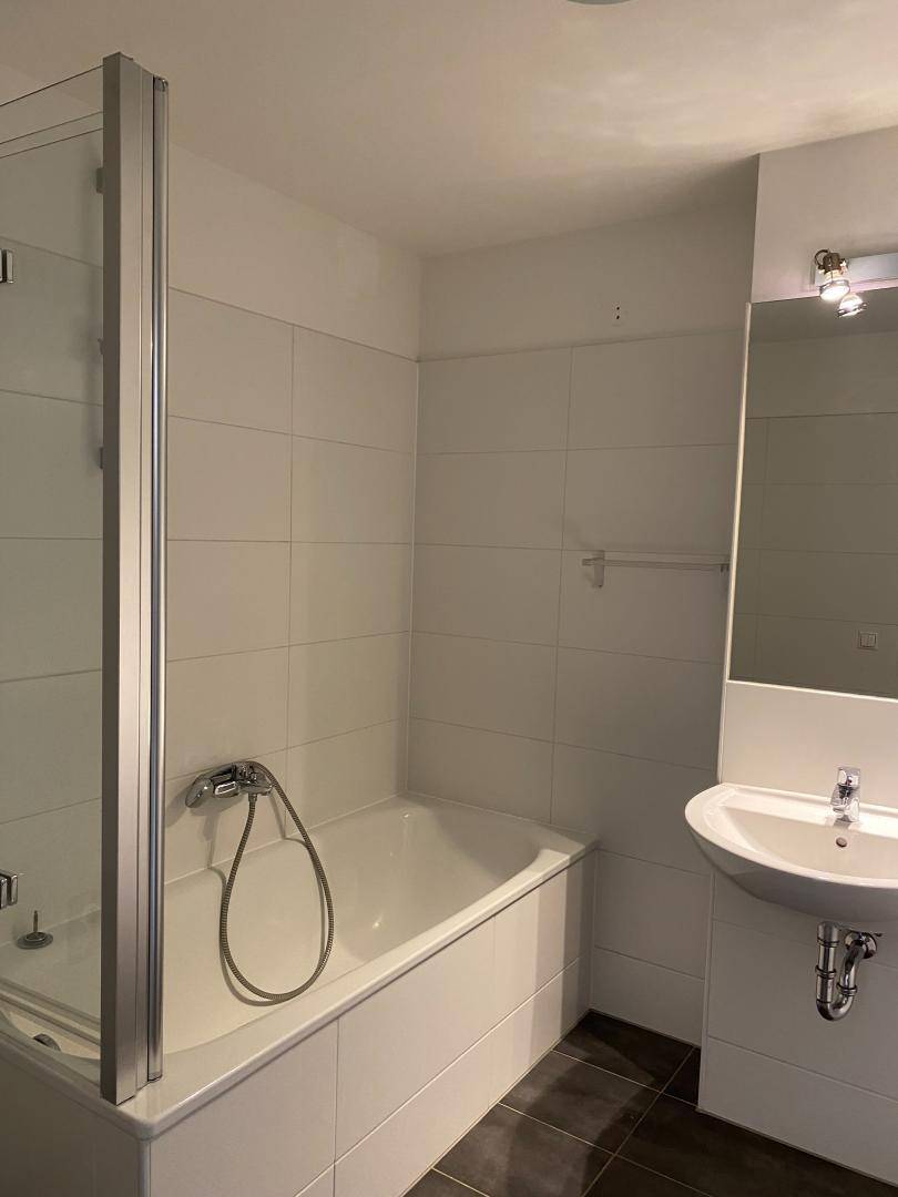 Modernes Badezimmer mit Badewanne, Duschabtrennung und weiß gefliesten Wänden, sehr sauber.