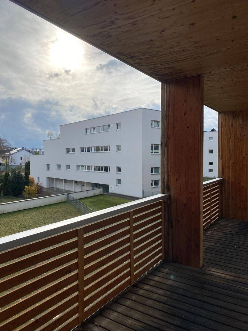 Sonniger Holzbalkon mit Blick auf die moderne Architektur und die grüne Umgebung, sehr hell.