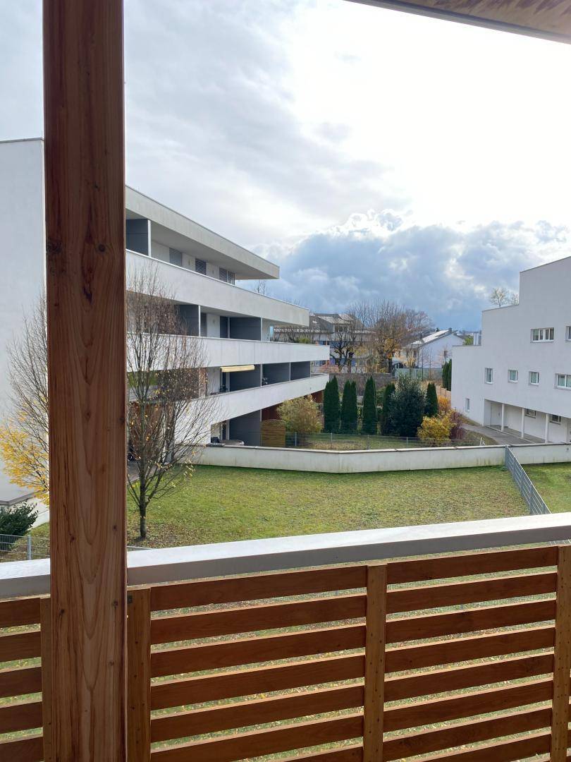 Balkon mit Holzboden und Geländer, bietet einen weiten Blick auf die Grünfläche und Gebäude.