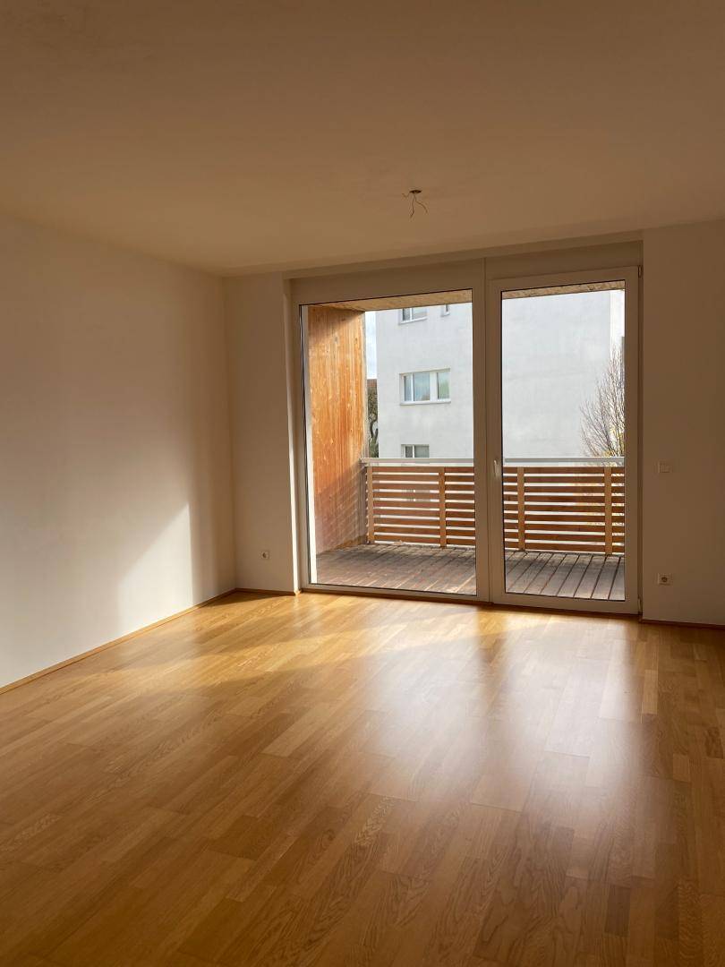 Lichtdurchfluteter Wohnbereich mit Holzboden und großem Fenster zum Balkon, sehr einladend.