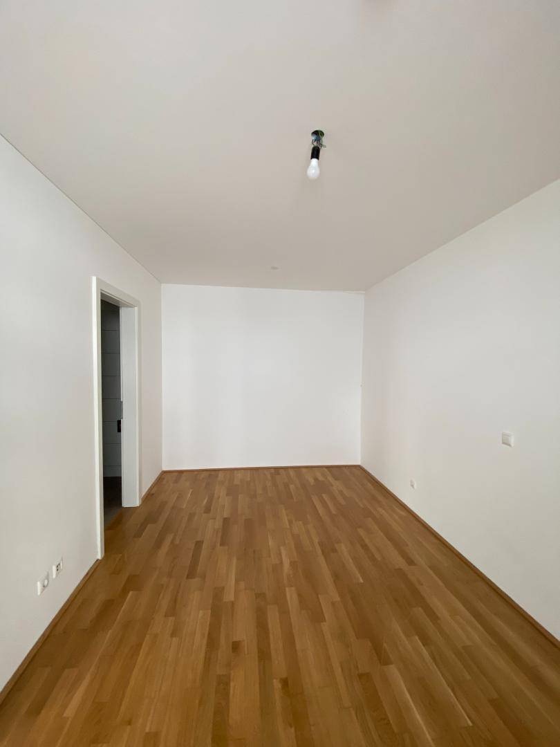 Leeres Schlafzimmer mit hellem Parkettboden und weiß gestrichenen Wänden, bietet viel Gestaltungspotenzial.