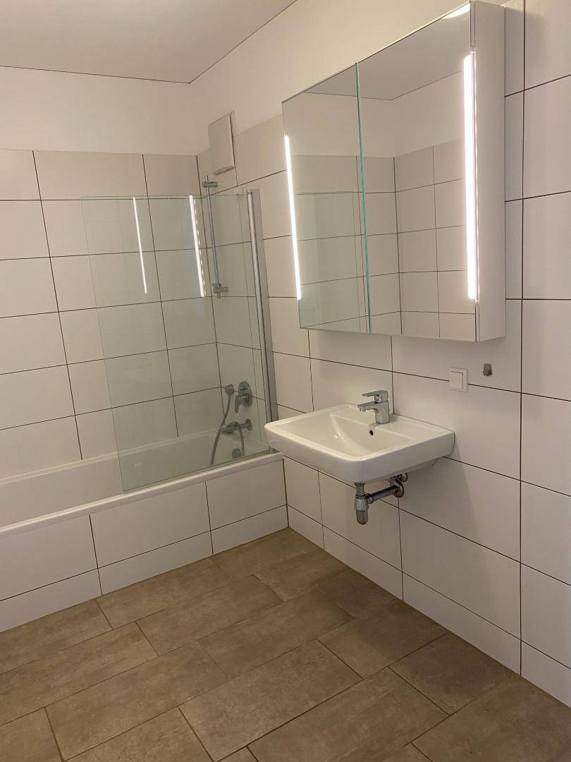 Modernes Badezimmer mit Badewanne, Duschabtrennung, Einzelwaschbecken und weiß gefliesten Wänden.