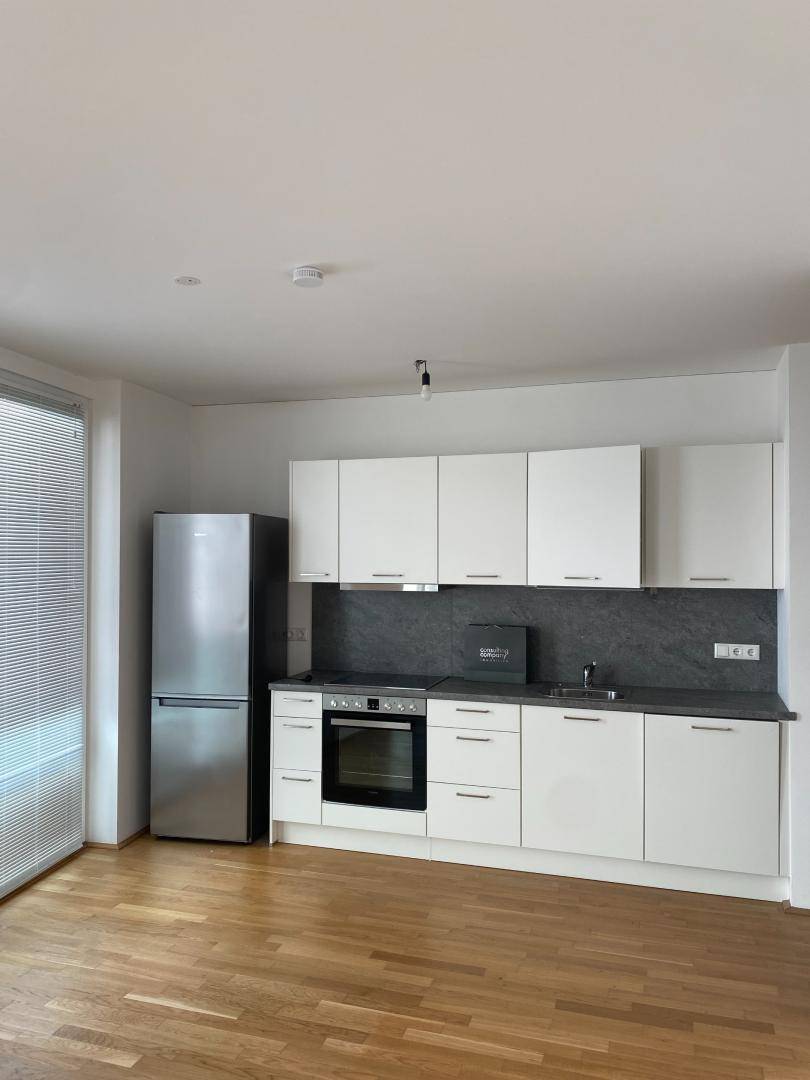 Moderne Einbauküche mit weißen Schränken, dunkler Arbeitsplatte und hellem Holzparkettboden.