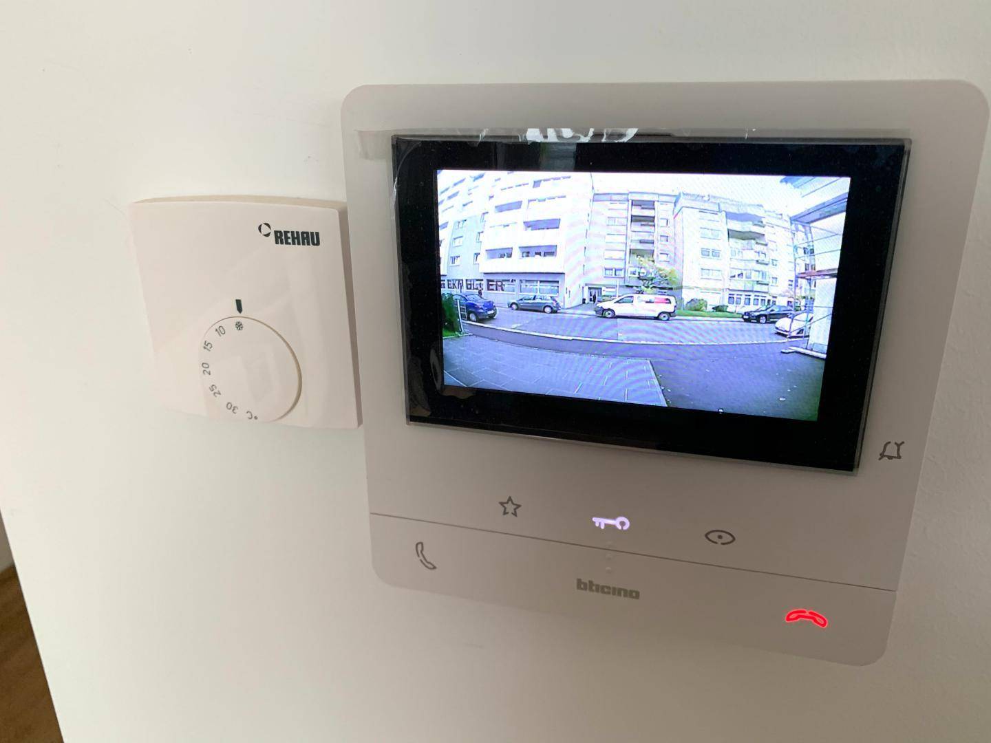 Moderne Gegensprechanlage mit Videofunktion und Thermostat an einer weißen Wand montiert.