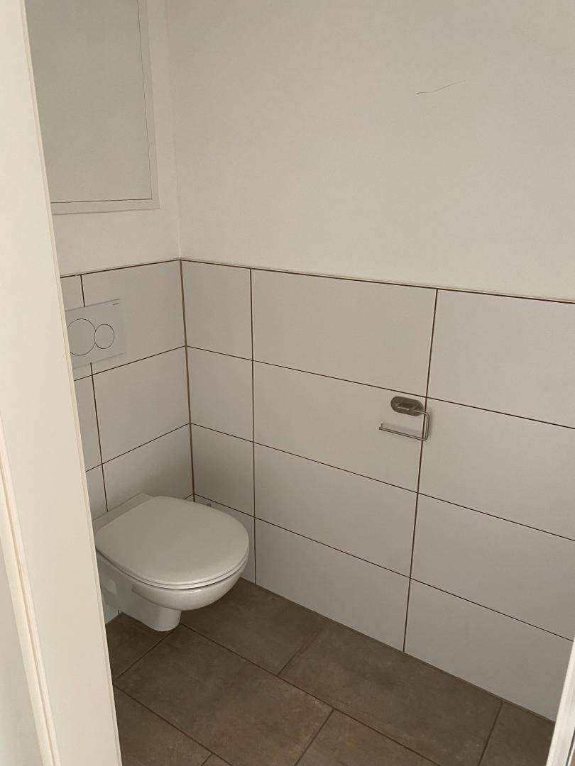 Separates Gäste-WC mit Wand-WC und hellen Fliesen an den Wänden, praktisch und funktional gestaltet.