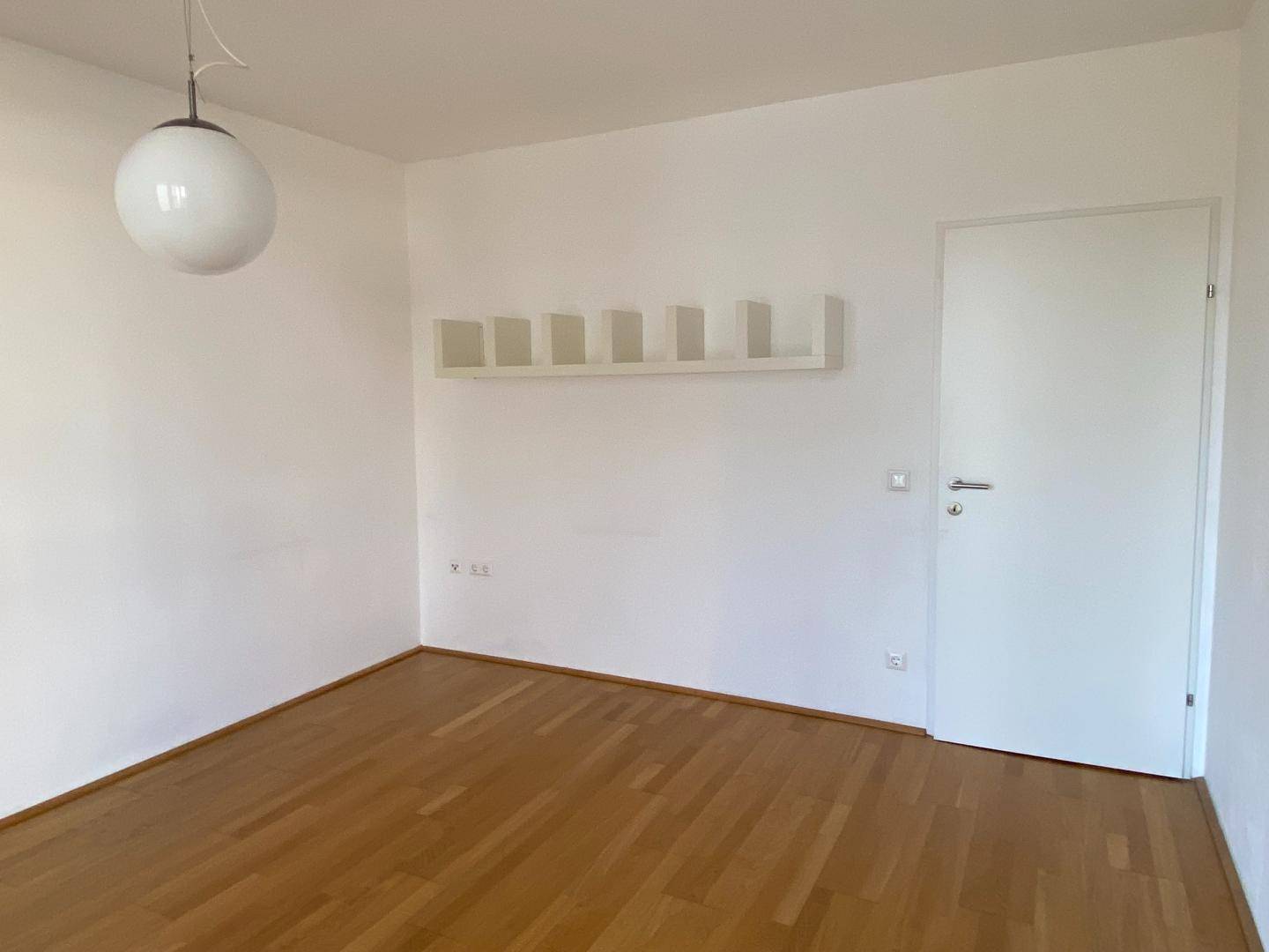Helles Schlafzimmer mit Parkettboden und weiß gestrichenen Wänden.