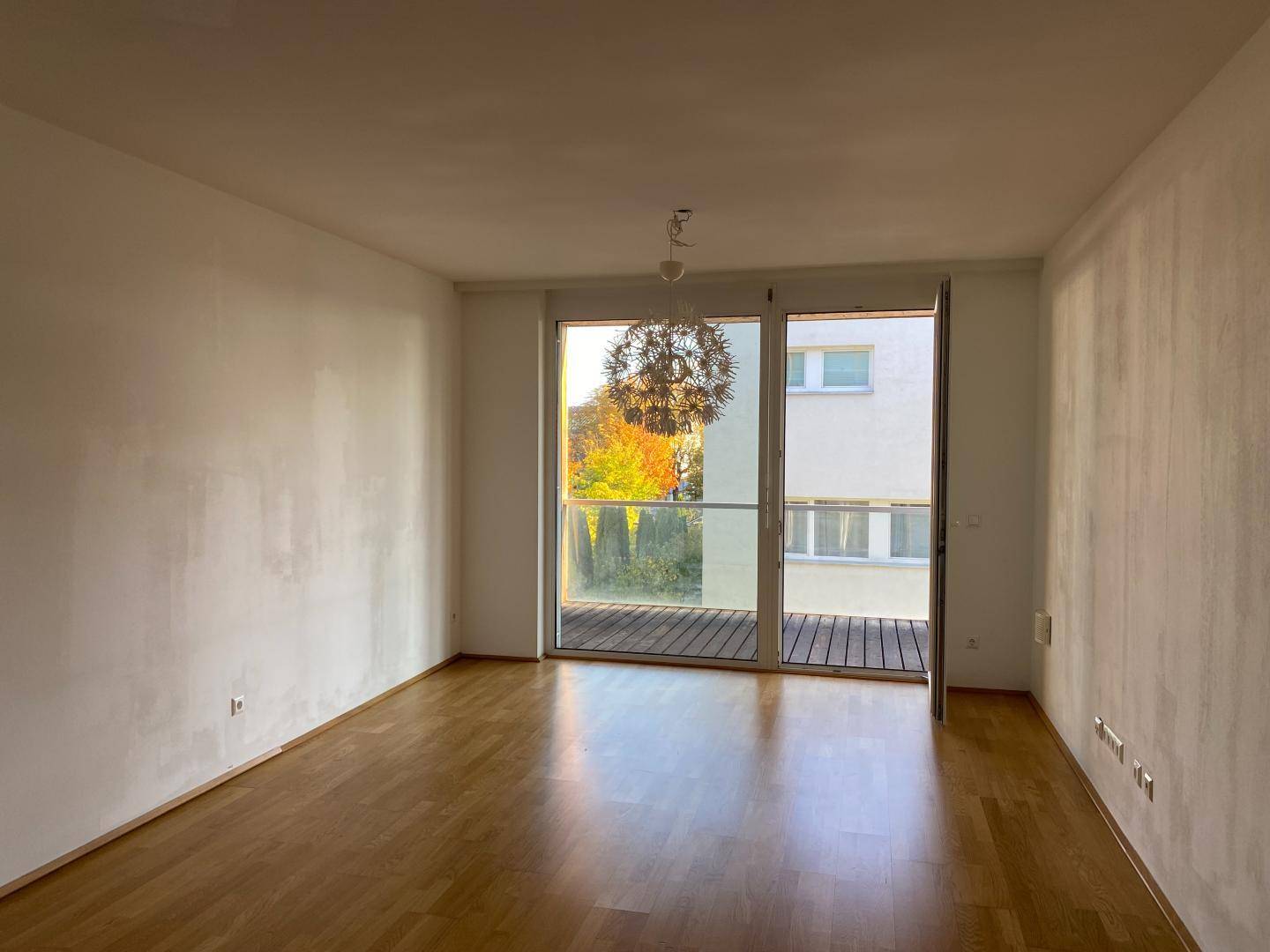 Helles Wohnzimmer mit Parkettboden, großen Fenstern und Zugang zu einem Balkon.