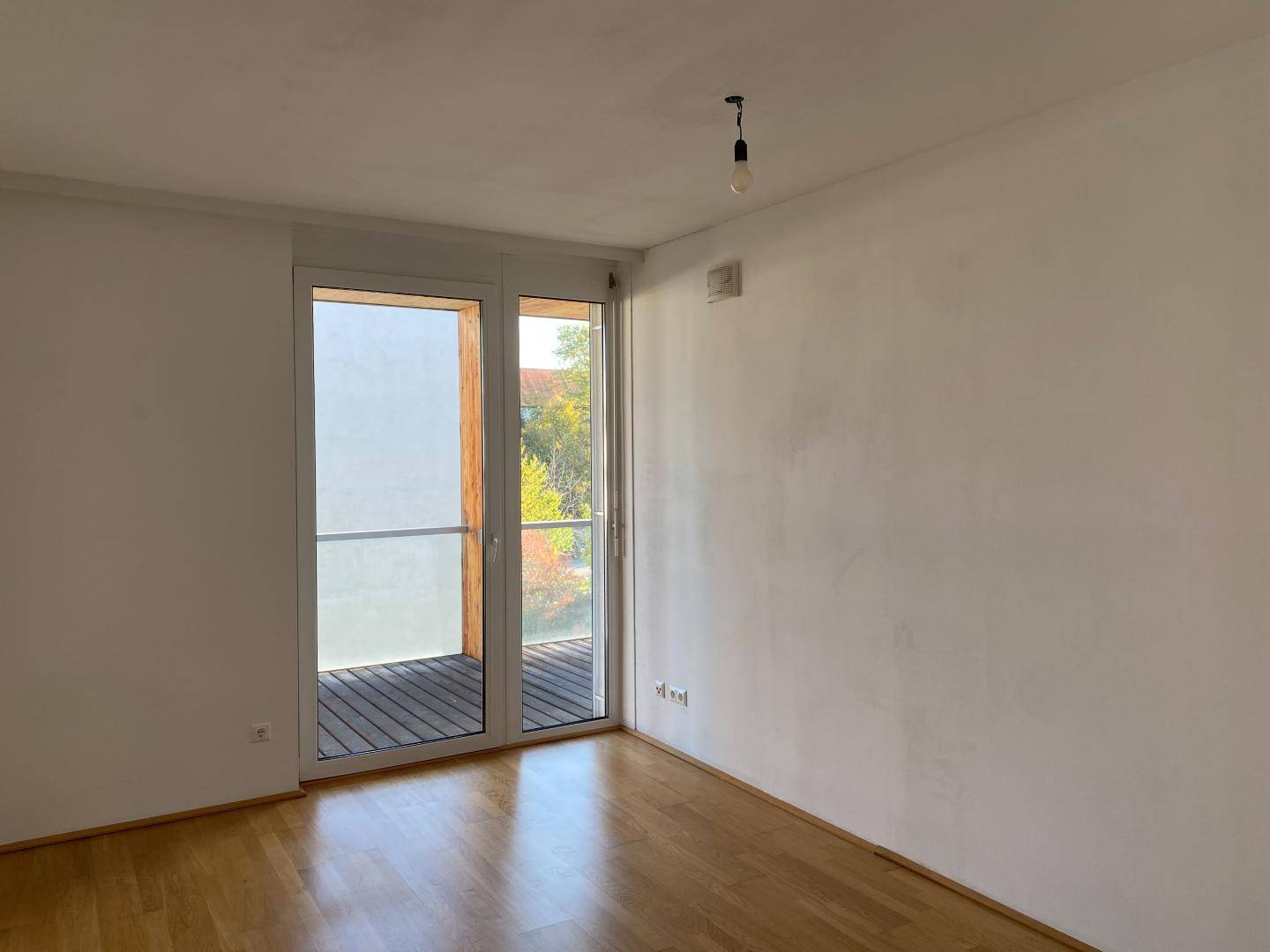 Heller Raum mit Parkettboden und Zugang zu einem Balkon, ideal als Schlaf- oder Arbeitszimmer.