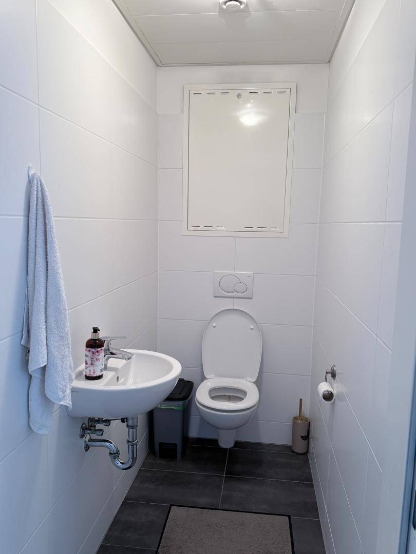 Separates Gäste-WC mit weißen Fliesen, Toilette und kleinem Handwaschbecken.