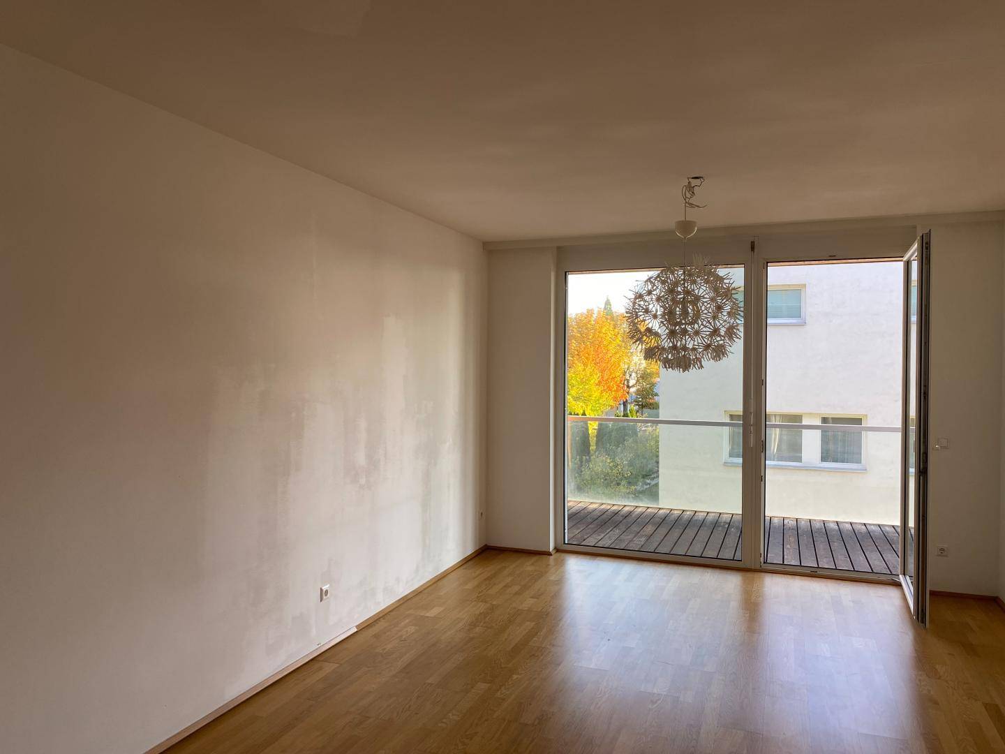 Lichtdurchfluteter Raum mit Holzboden und breiter Balkontür, ideal als Wohnbereich.