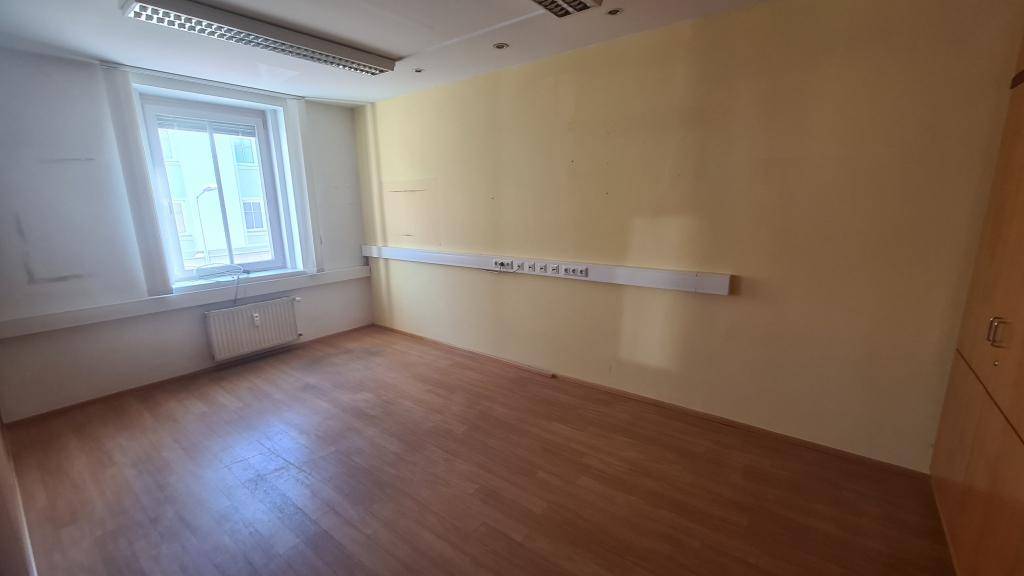 Büro mit Holzboden, großem Fenster und gelber Akzentwand, ausgestattet mit vielen Steckdosen.