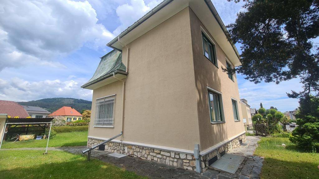 Seitenansicht des Hauses mit beigefarbener Fassade, Steinsockel und Zugang zum Gartenbereich.
