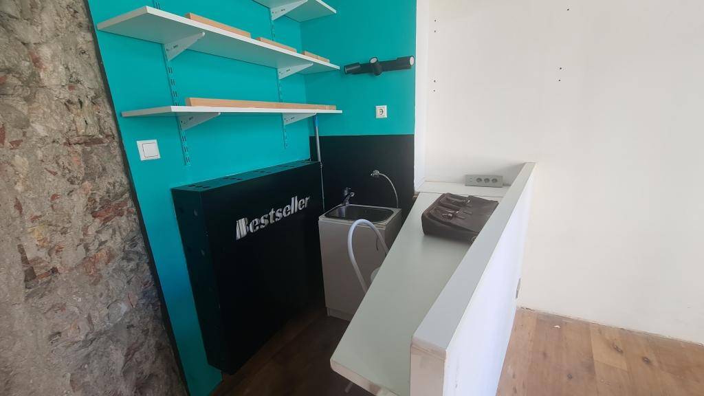 Kleine Küchenzeile mit Spülbecken und Regalen an einer türkisen Wand in einem Geschäftsraum.