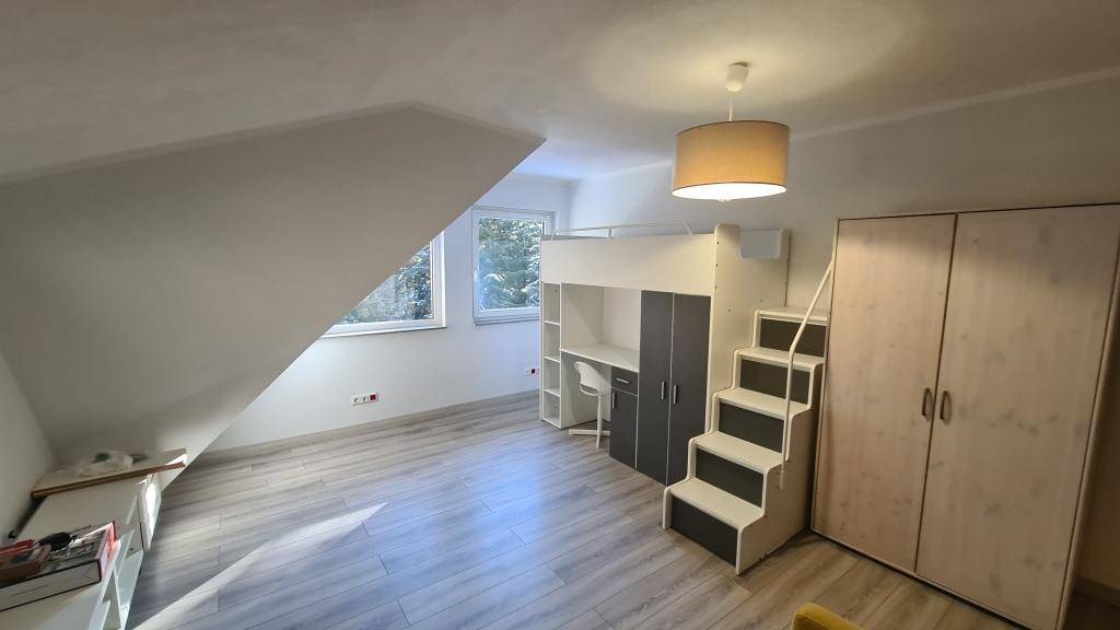 Geräumiges Dachgeschoss-Schlafzimmer mit Hochbett, Schreibtisch und Kleiderschrank.