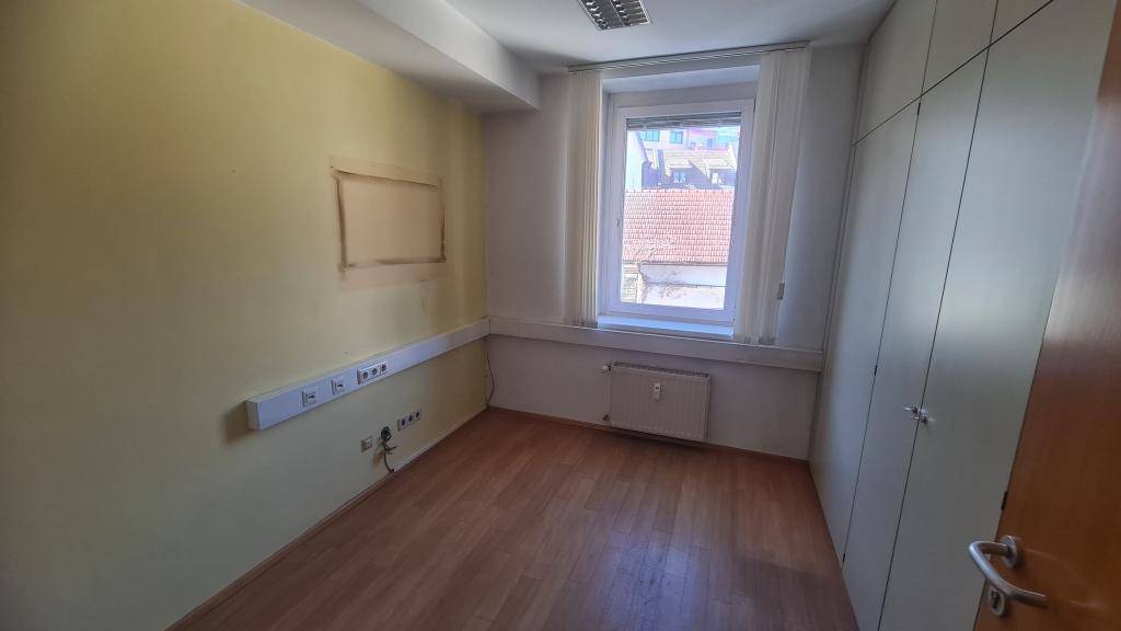 Büro mit Holzboden, Fenster und Einbauschränken, mit Blick auf die Dächer der Umgebung.