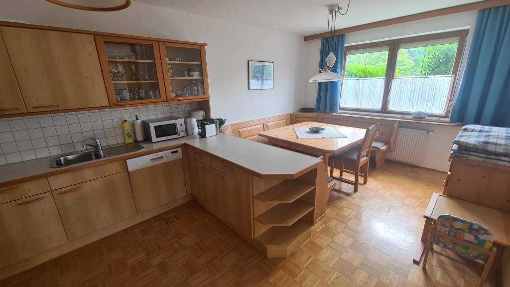 Geräumige Wohnküche mit Holzeinrichtung, Essecke und Fenster mit Blick ins Grüne.