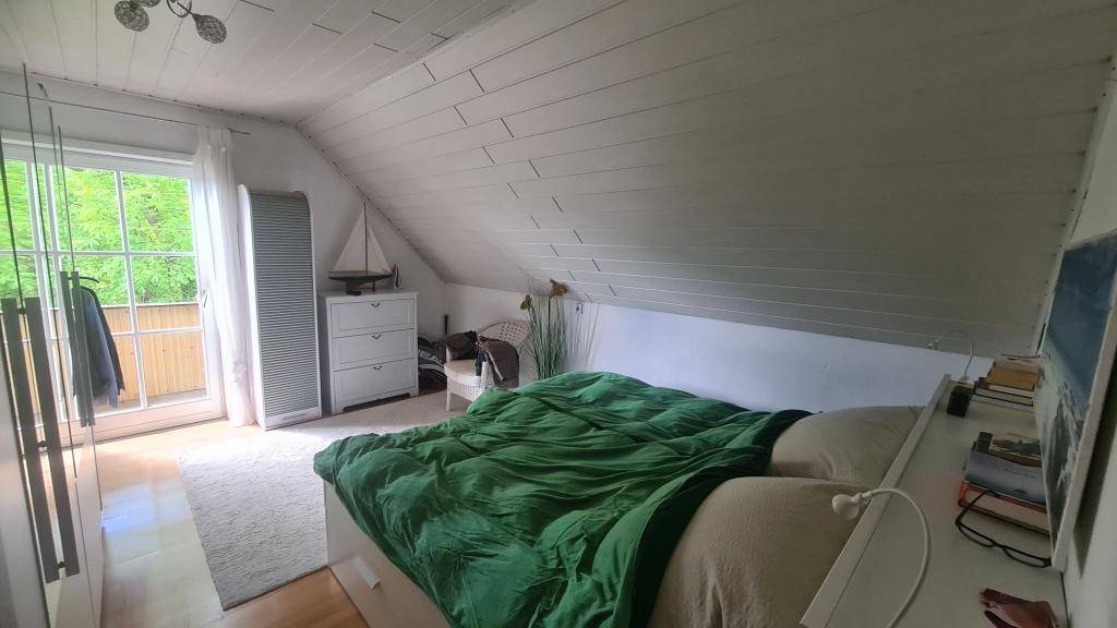 Gemütliches Schlafzimmer im Dachgeschoss mit Holzboden und Zugang zum Balkon.
