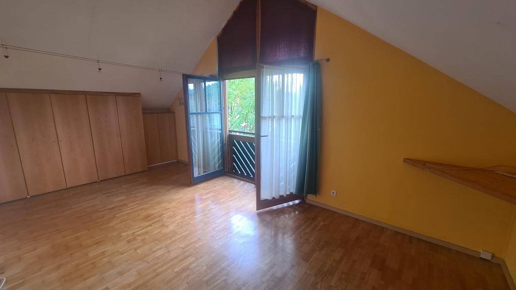 Schlafzimmer im Dachgeschoss mit Holzparkettboden, farbigen Wänden und Balkonzugang.