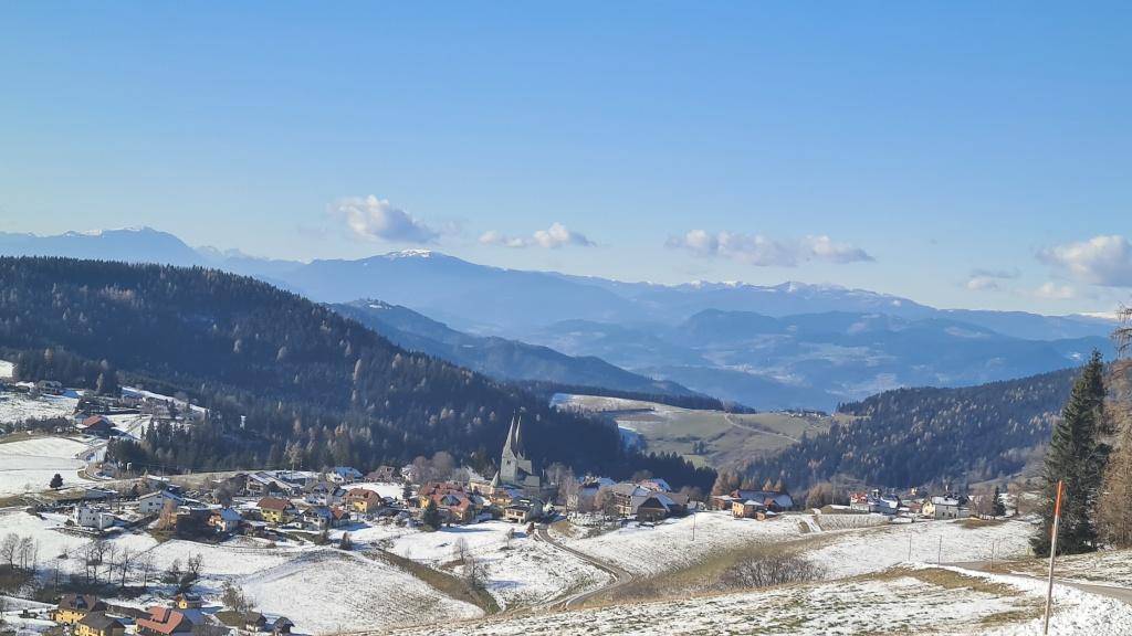 Weitläufiger Blick über eine verschneite Landschaft mit Bergen und einem malerischen Dorf.