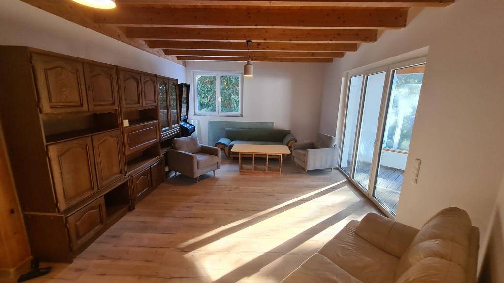Helles Wohnzimmer mit Holzboden, großen Fenstern und Zugang zu einem Balkon.