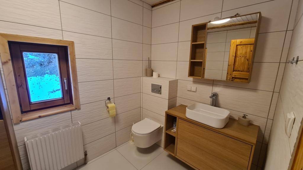 Modernes Badezimmer mit weißen Fliesen, Holzwaschtisch, Wand-WC und Fenster.