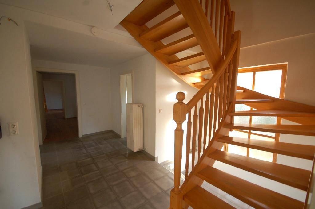 Heller Flur mit Holztreppe und Fliesenboden, der die Stockwerke verbindet.