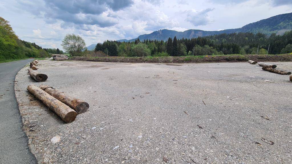 Weitläufiges Schotterfeld mit Baumstämmen als Begrenzung und Bergpanorama im Hintergrund.