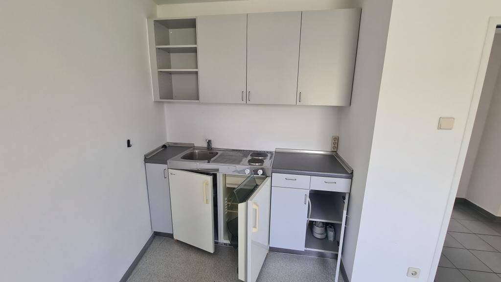 Kleine Küchenzeile mit grauen Schränken, Spüle, zwei Kochplatten und einem Kühlschrank, ideal für kleine Räume.