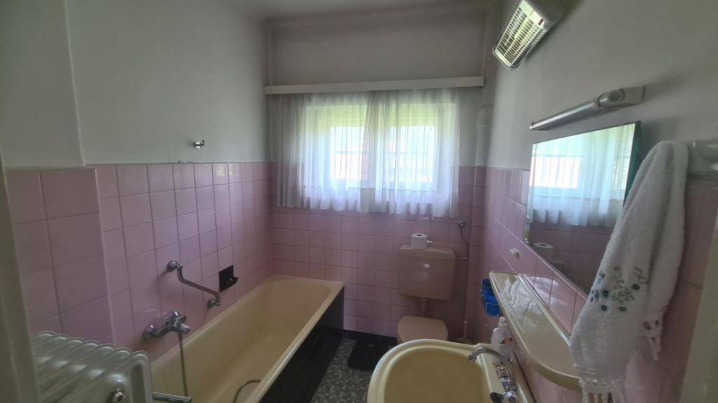 Badezimmer mit rosa Fliesen, Badewanne und Fenster, im Stil der 80er Jahre.