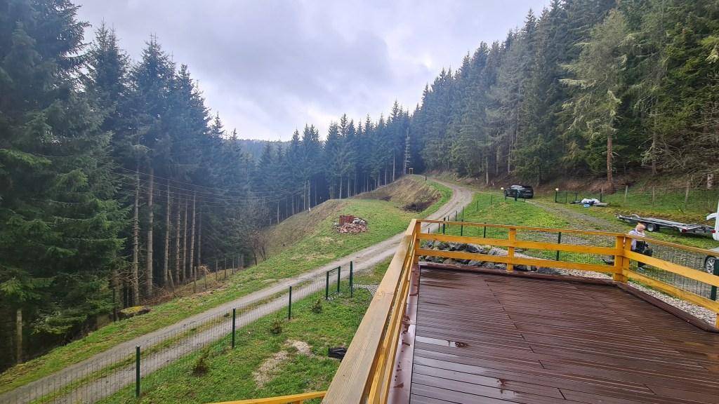 Holzterrasse mit weitem Blick auf den Wald und eine unbefestigte Straße in der Natur.