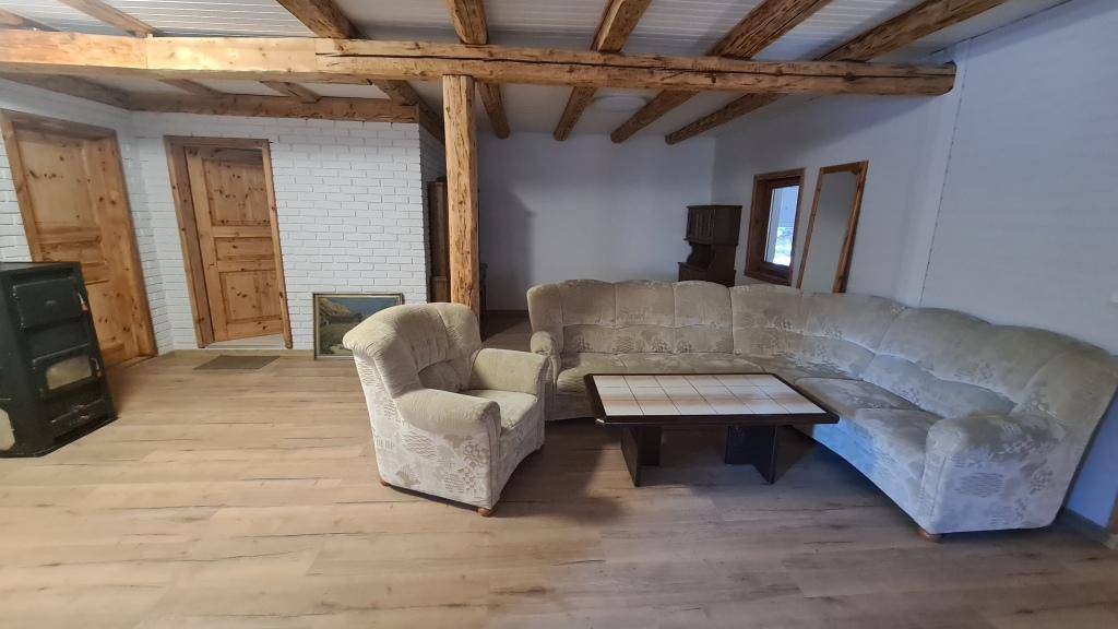 Wohnzimmer mit Ecksofa, sichtbaren Holzbalken und einem Kaminofen, bereit zur Einrichtung.