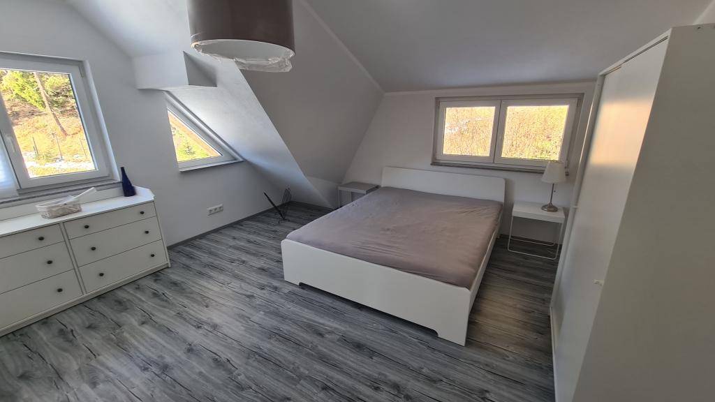 Dachgeschoss-Schlafzimmer mit Schrägen, Holzboden und einem schönen Blick ins Grüne.