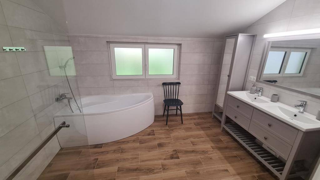 Modernes Badezimmer mit Eckbadewanne, Doppelwaschbecken und Holzoptikfliesen.