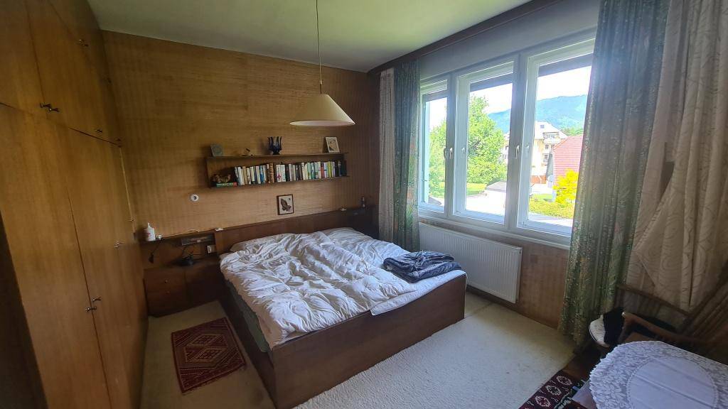 Schlafzimmer mit Holzwänden, Doppelbett und großem Fenster mit Blick ins Grüne.