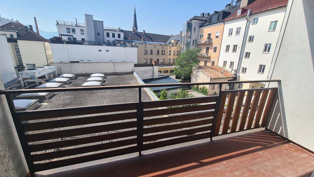 Balkon mit Holz- und Metallgeländer, bietet einen Panoramablick über die Dächer der Stadt und eine Kirchturmspitze.