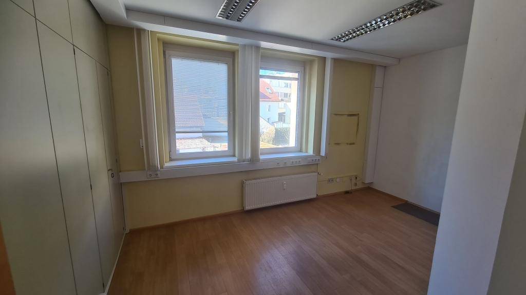 Büro mit Holzboden, zwei Fenstern und Einbauschränken, bietet viel Tageslicht und Stauraum.