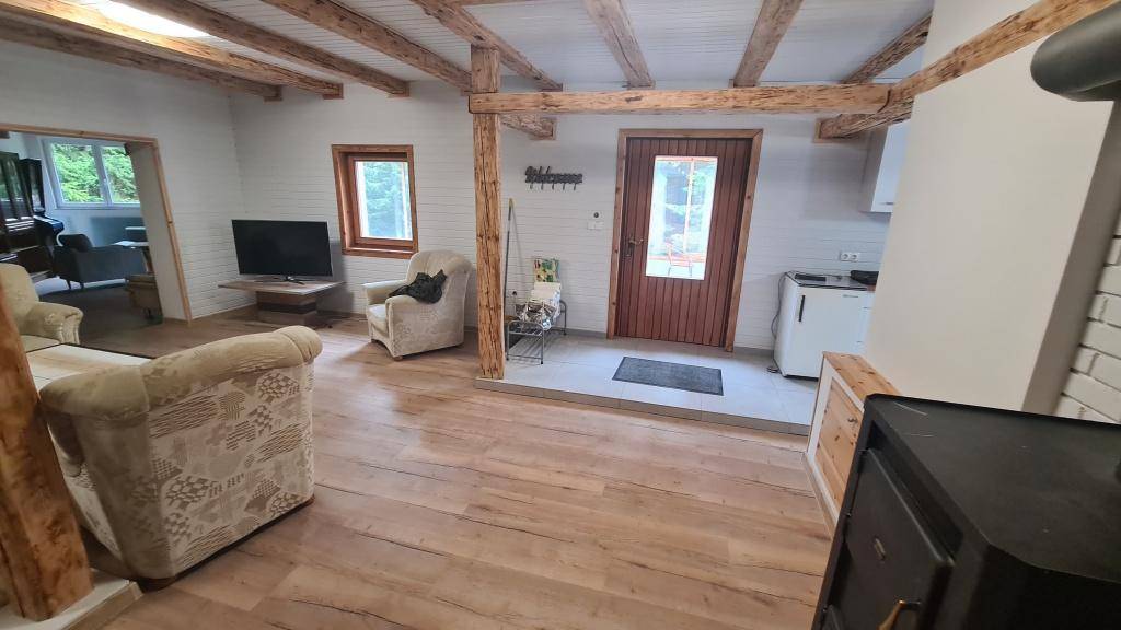 Gemütliches Wohnzimmer mit sichtbaren Holzbalken, Holzboden und einem Kaminofen.