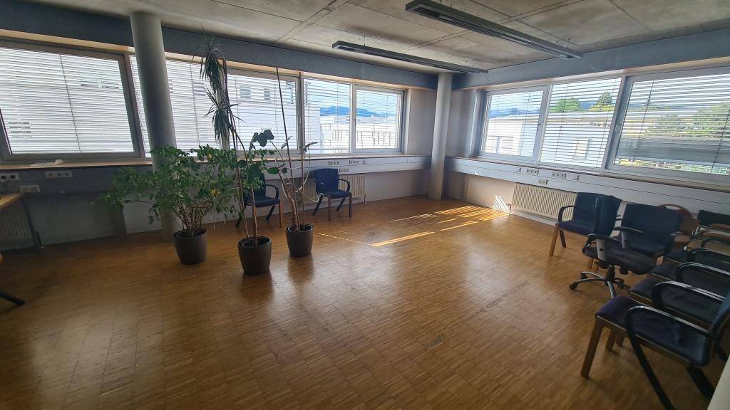 Heller und geräumiger Büroraum mit Holzparkettboden, großen Fenstern und viel natürlichem Licht, ideal für Arbeitsbereiche.